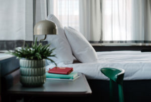 hotellrum-närbild-på-säng-med-fönster-i-bakrunden-ett-skrivbord-med-stol-och-bordslampa
